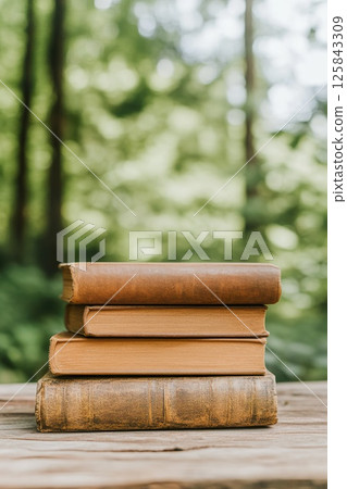 Stack of vintage books outdoors with natural green background. 125843309