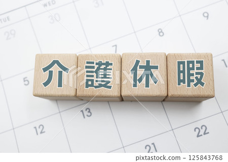 A wooden block with the words "Caregiver Leave" written on it is placed on a calendar 125843768