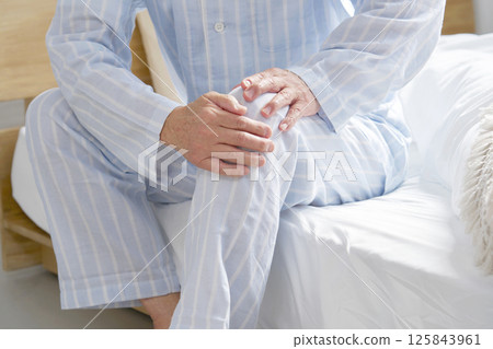 Middle-aged man in pajamas with knee pain, no face 125843961