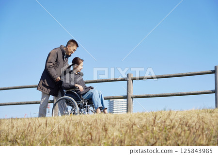 A husband taking a walk pushing his wife's wheelchair 125843985