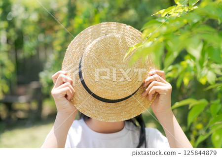 Girl hiding her face with a straw hat 125844879