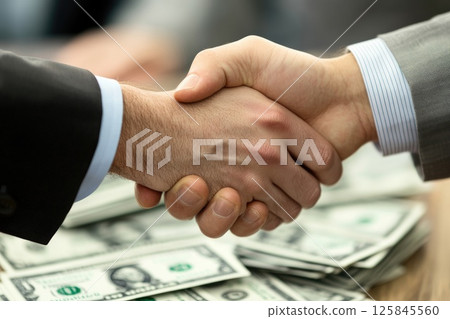 Two men shaking hands over a pile of money. Concept of trust and agreement between the two men 125845560