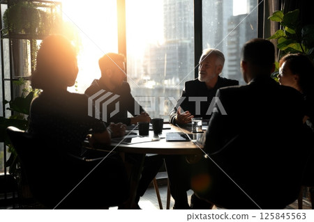 Business Team Discussion Around Round Table with Natural Light and City Background 125845563