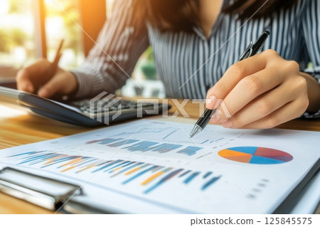 Business Executive Working in a Sleek Modern Office with Reports and Calculator Business Executive Working in a Sleek Modern Office with Reports and Calculator 125845575