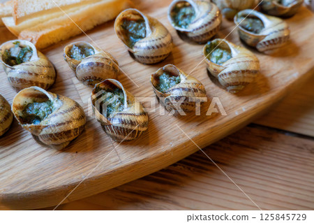 Escargot with garlic butter on wooden platter 125845729