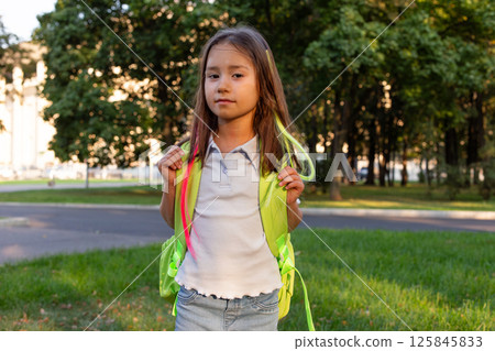 Young girl in park wearing bright green backpack on sunny day Young girl in park wearing bright green backpack on sunny day 125845833