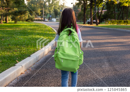 Young girl walking to school with green backpack on a tranquil street Young girl walking to school with green backpack on a tranquil street 125845865