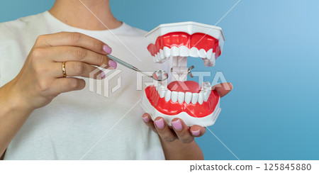Female holding dental model with mirror for oral health education on blue background Female holding dental model with mirror for oral health education on blue background 125845880