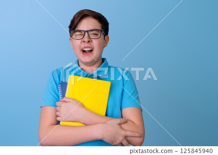 Caucasian Teen Boy with glasses with colorful laptops in a blue shirt, yawns with fatigue Caucasian Teen Boy with glasses with colorful laptops in a blue shirt, yawns with fatigue 125845940