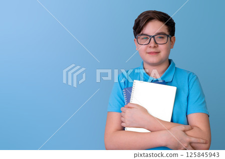 Young caucasian male teen holding notebooks in blue polo against solid background 125845943