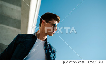 Young Man Wearing Sunglasses by a Concrete Wall Under Clear Blue Sky During Sunny Day 125846341
