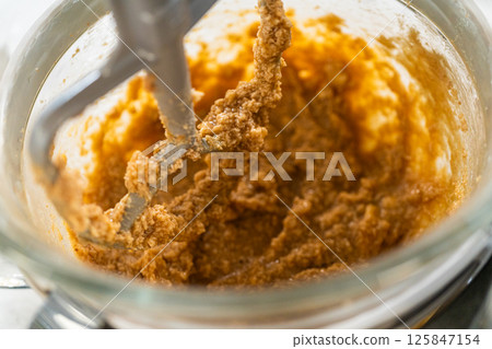 Close-up view of the stand mixer blending the dough mixture to a smooth consistency, capturing the dough as it adheres to the mixing attachment in the Amber Gingerbread Cookie Dough process. The dough Close-up view of the stand mixer blending the dough mixture to a smooth consistency, capturing the dough as it adheres to the mixing attachment in the Amber Gingerbread Cookie Dough process. The dough 125847154