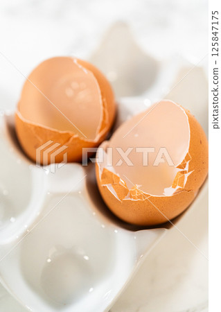 Close-up of two cracked eggshells, showing the remnants of eggs used in the Chocolate Ginger Sugar Cookie Dough recipe, symbolizing the baking process. 125847175