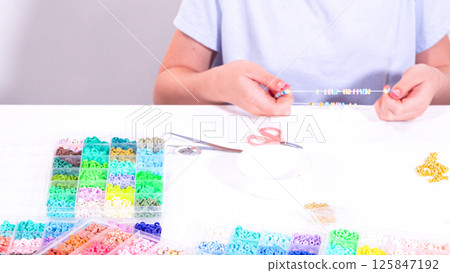 Delicate fingers of a young girl navigate through a treasure trove of bright, multicolored beads, each compartment revealing a new hue to choose from. 125847192