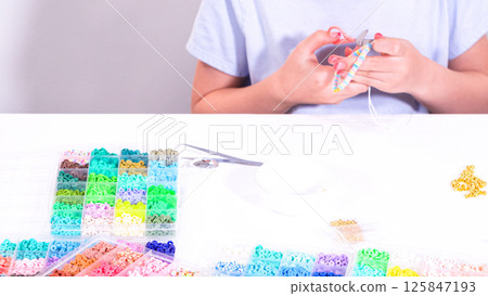 Delicate fingers of a young girl navigate through a treasure trove of bright, multicolored beads, each compartment revealing a new hue to choose from. 125847193