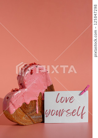 LOVE YOURSELF words on paper note card Valentine's Day holiday idea Heart shaped strawberry berry croissant on pink background with copy space. Puff pastry new trendy sweet dessert bakery. Creamy 125847298
