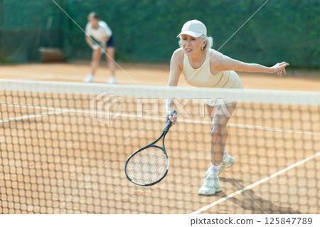 Senior female athlete plays tennis on open court with young opponent 125847789