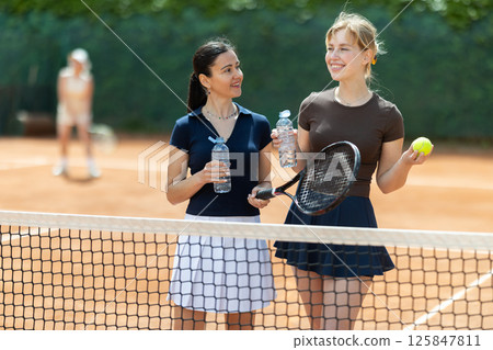 Adult and young women chatting on tennis court Adult and young women chatting on tennis court 125847811