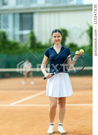 Woman in sportswear against backdrop of outdoor tennis court. 125847836