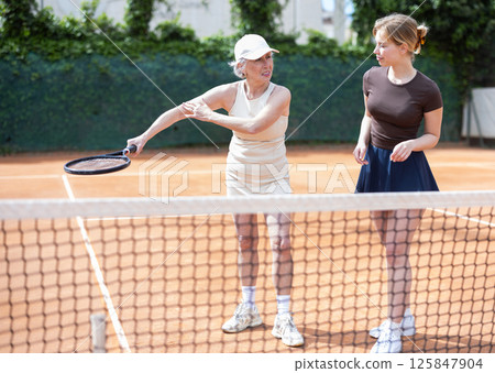 Elderly woman teaches young woman to play tennis 125847904