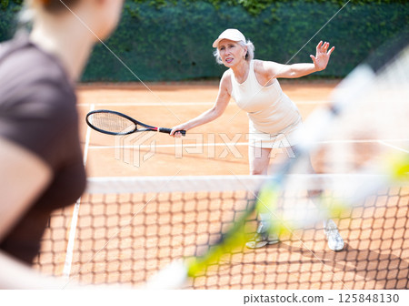 Elderly woman plays tennis on tennis court 125848130