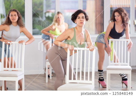 Woman stands next to chair, leans on back and performs set of lap dance movements 125848149