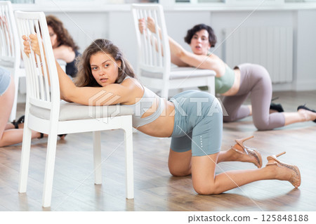 Young woman kneeling on floor during sensual lap dance with chair in group studio Young woman kneeling on floor during sensual lap dance with chair in group studio 125848188