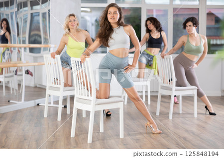 Young woman in stiletto heels performing sass dance with chair in studio 125848194