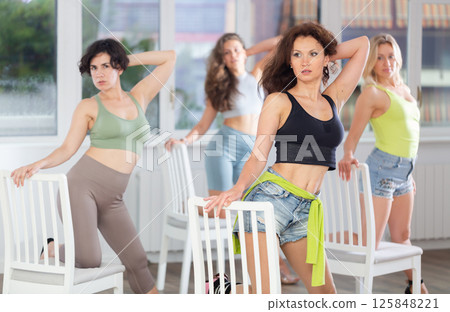Group of women in high heels rehearsing dance while leaning on chair 125848221