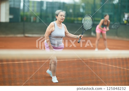 Young and elderly women playing doubles tennis 125848232