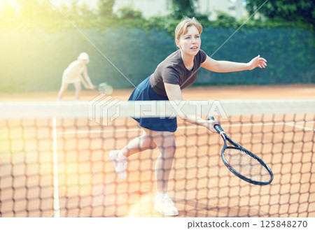 Middle aged and senior women plays tennis on open court with opponent. Middle aged and senior women plays tennis on open court with opponent. 125848270