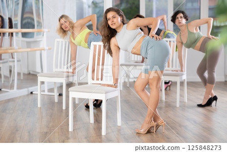 Young woman in high heels performing sensual dance on chair during group class 125848273