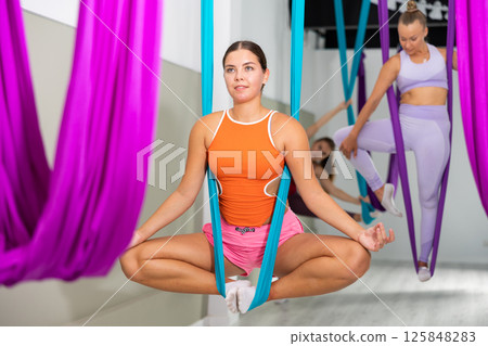 Girl sitting in butterfly pose in suspended hammock with fingers folded in mudra 125848283