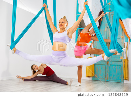 Sporty woman doing split on hanging hammocks during aerial yoga training Sporty woman doing split on hanging hammocks during aerial yoga training 125848329