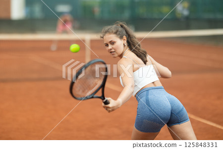 Enthusiastic sporty girl playing tennis on outdoor court Enthusiastic sporty girl playing tennis on outdoor court 125848331