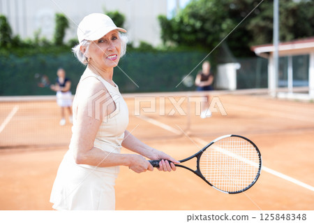 Elderly woman playing doubles tennis on court 125848348