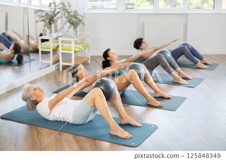 Elderly woman doing pilates with soft ball in group 125848349