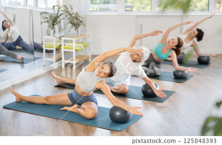 Group of women of different ages practicing yoga or pilates with balls in the gym of modern fitness studio. 125848393