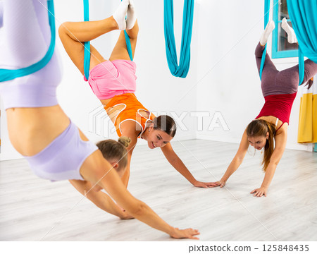 Group of women hang upside down in a hammock. Fly yoga class in gym. Fit and wellness lifestyle Group of women hang upside down in a hammock. Fly yoga class in gym. Fit and wellness lifestyle 125848435
