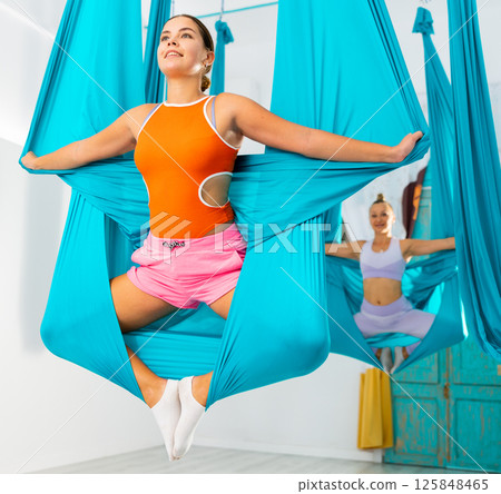 Young women making antigravity yoga exercises with group of people 125848465