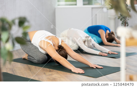 Women of different ages resting in kneeling asana Balasana child pose during group yoga class in studio Women of different ages resting in kneeling asana Balasana child pose during group yoga class in studio 125848470