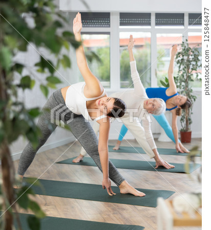 Group of active women practices the Parivritta Trikonasana pose Group of active women practices the Parivritta Trikonasana pose 125848477