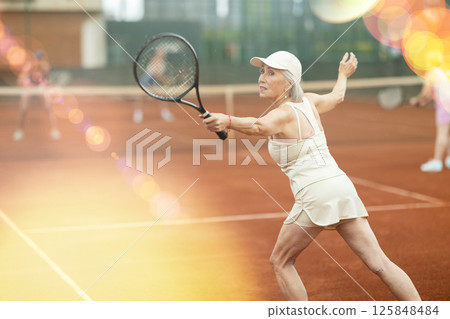 Sporty senior woman playing doubles tennis on summer court Sporty senior woman playing doubles tennis on summer court 125848484