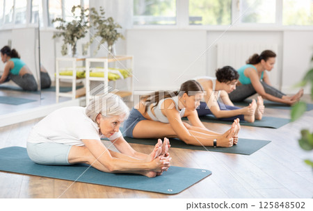 Senior woman stretching into Paschimottanasana during group yoga session 125848502