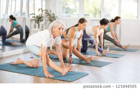 Elderly woman stretching in Half Monkey Pose in yoga class 125848505