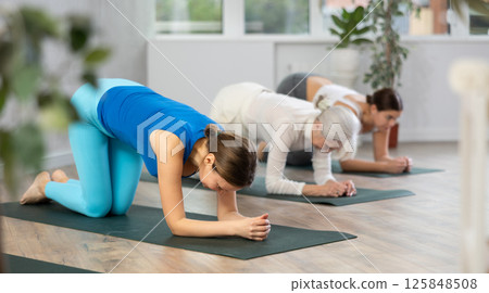 Sportive women of different ages performing various stretching exercises during yoga workout in studio 125848508