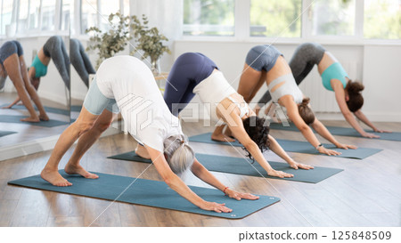 Elderly woman performing Adho Mukha Svanasana at group yoga class 125848509