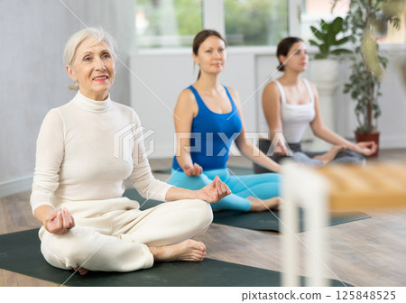 Diligent women practicing lotus pose of yoga in light fitness room 125848525