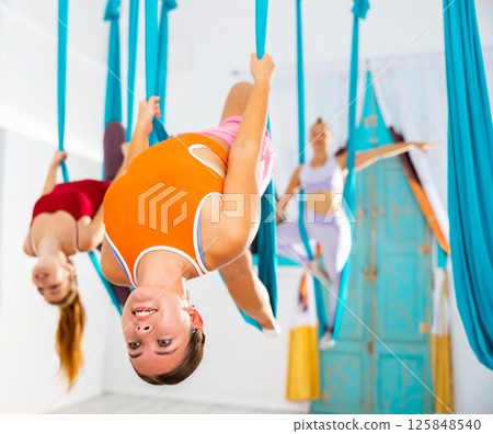 Group of women hang upside down in a hammock. Fly yoga class in gym. Fit and wellness lifestyle Group of women hang upside down in a hammock. Fly yoga class in gym. Fit and wellness lifestyle 125848540
