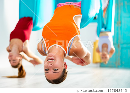 Girl doing dove pose during aerial yoga group training Girl doing dove pose during aerial yoga group training 125848543